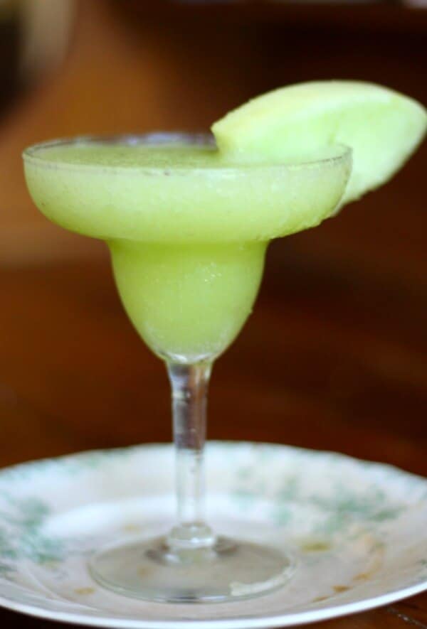 A margarita glass with light green honeydew margarita in it.