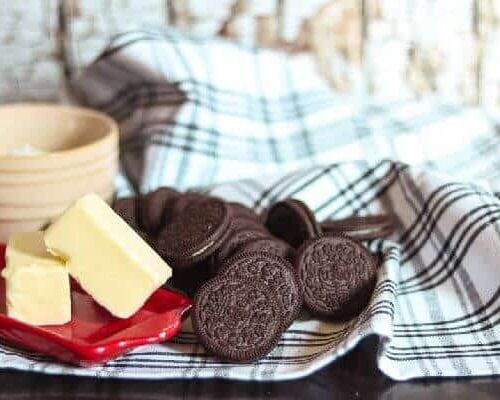 A stick of butter, Oreo cookies, and a bowl on a black and white towel.