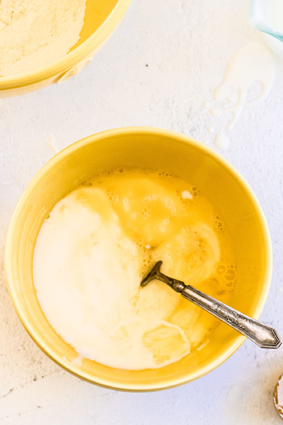 Overhead view of a bowl with buttermik, eggs, butter, and bacon grease.