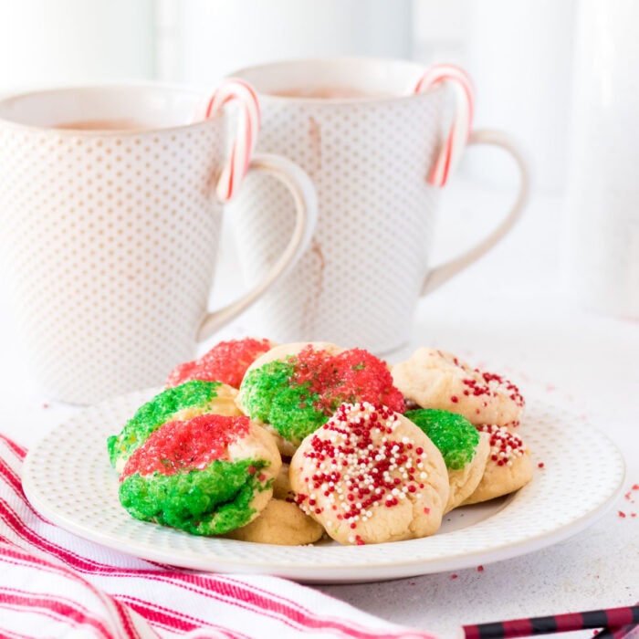 A plate of cookies with coffee cups in the background.