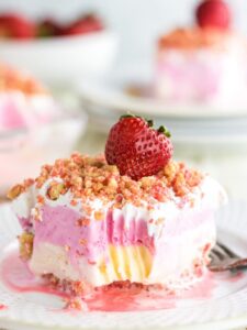 A closeup of a slice of strawberry crunch ice cream cake with a strawberry on top.