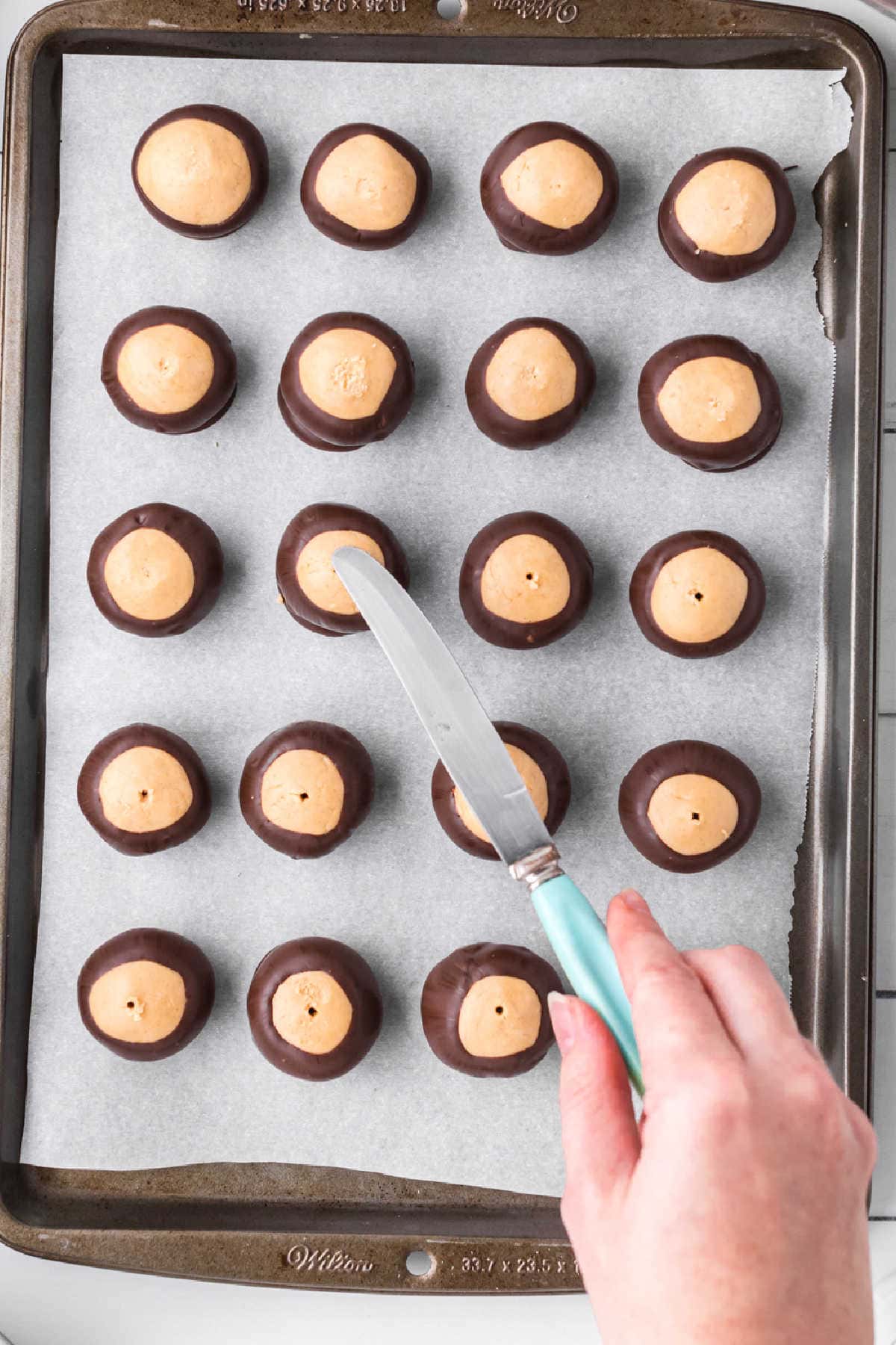 Smoothing the tops of the peanut butter balls dipped in chocolate.