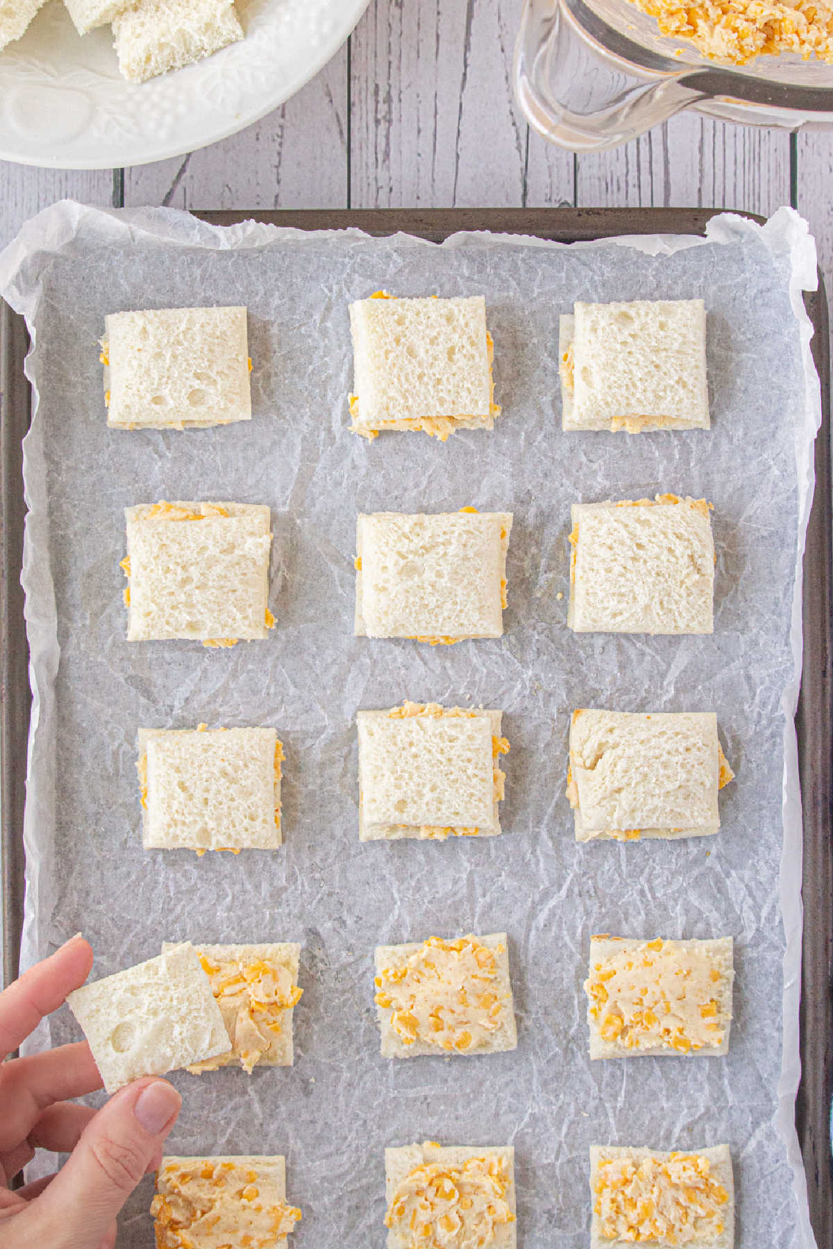 Cheese spread between two bread squares on a cookie sheet.