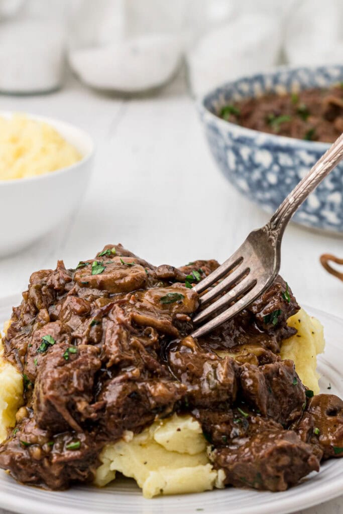 Beef tips and gravy over mashed potatoes with a fork in it.