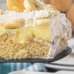 Close up of a piece of banana pudding poke cake with layers of cake, pudding, bananas, and Cool Whip. Text overlay for Pinterest.