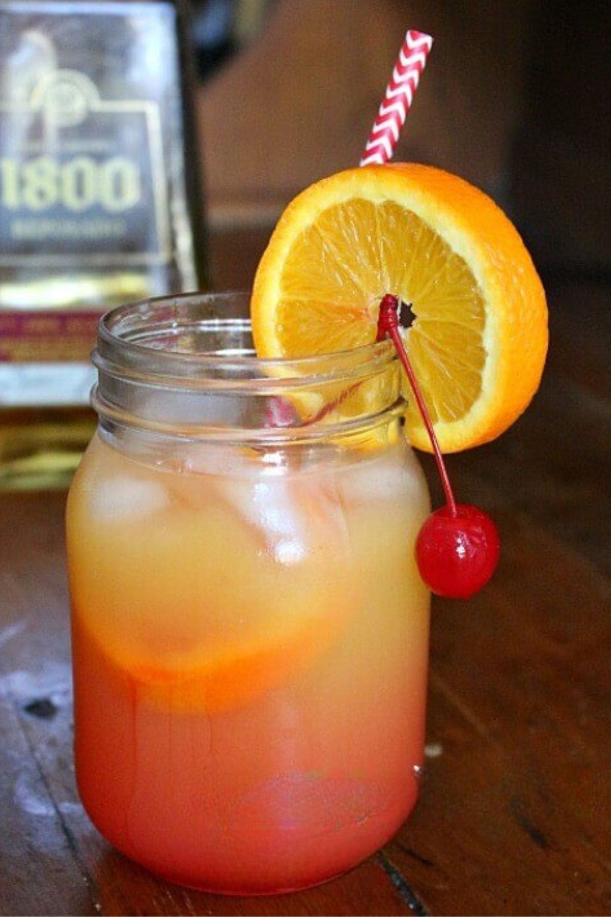 Closeup of the mango tequila sunrise garnished with a cherry and an orange wheel.