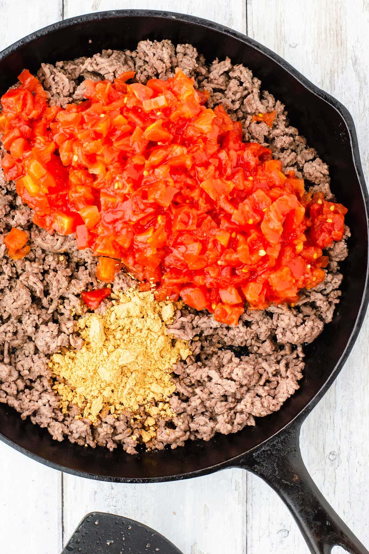 Skillet with cooked ground beef and tomatoes.