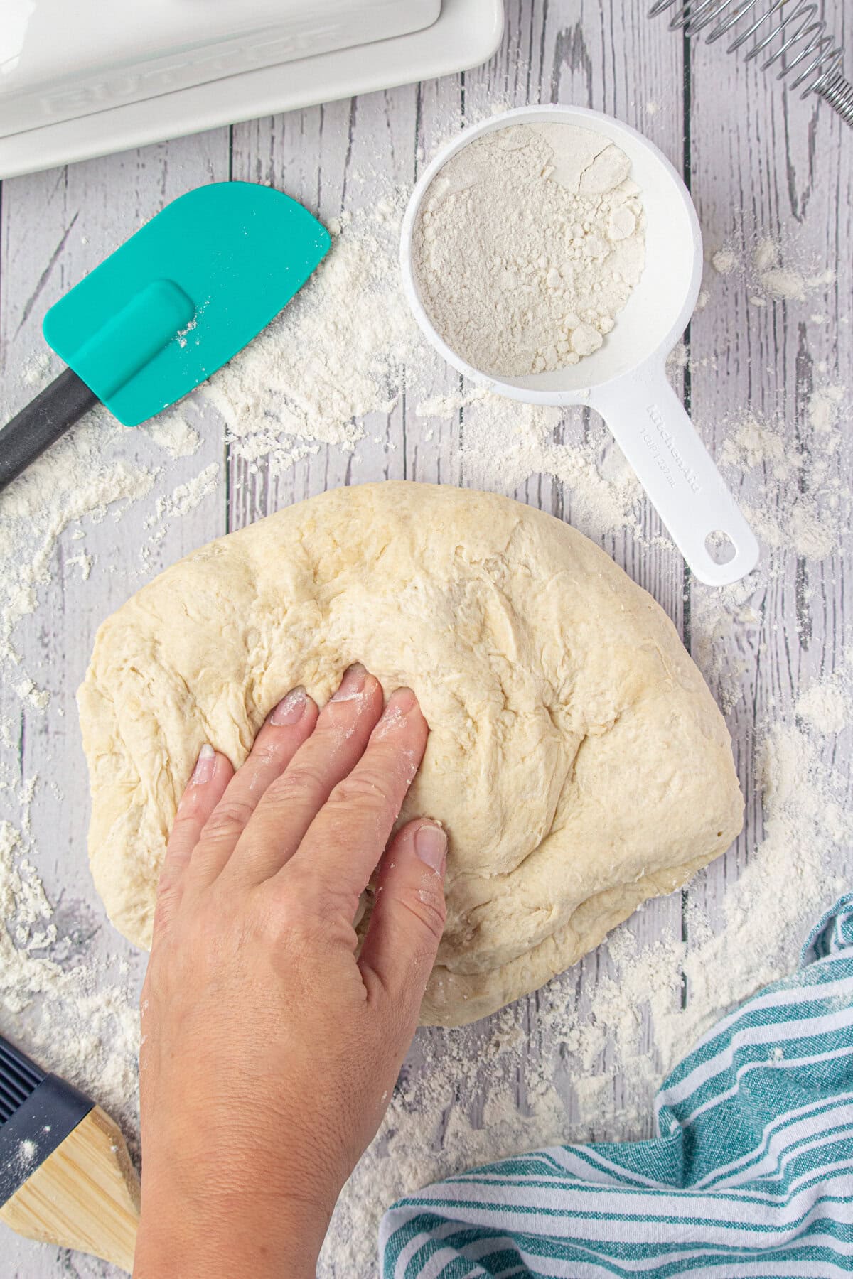 A hand kneading the dough on a floured countertop.