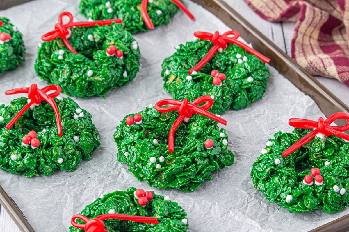 Cornflake Christmas wreath cookies decorated on a wax paper-covered baking sheet.