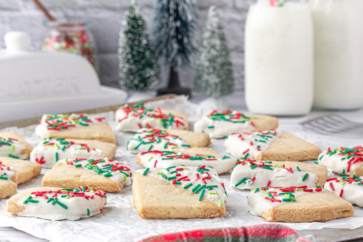 A side-angle view of Hawaiian shortbread cookies with sprinkles and Christmas decor in the background.