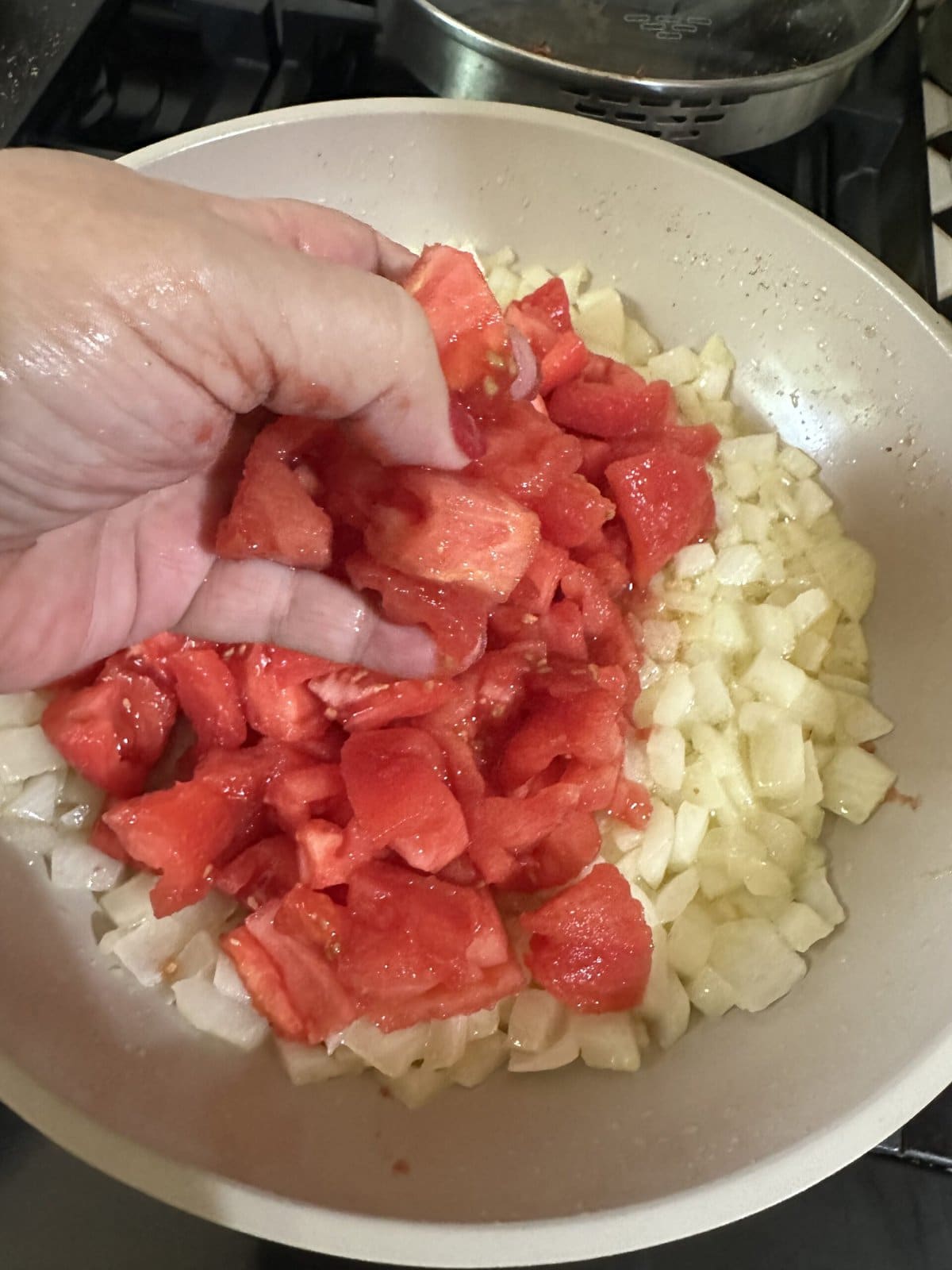 Adding the tomatoes to the onions.