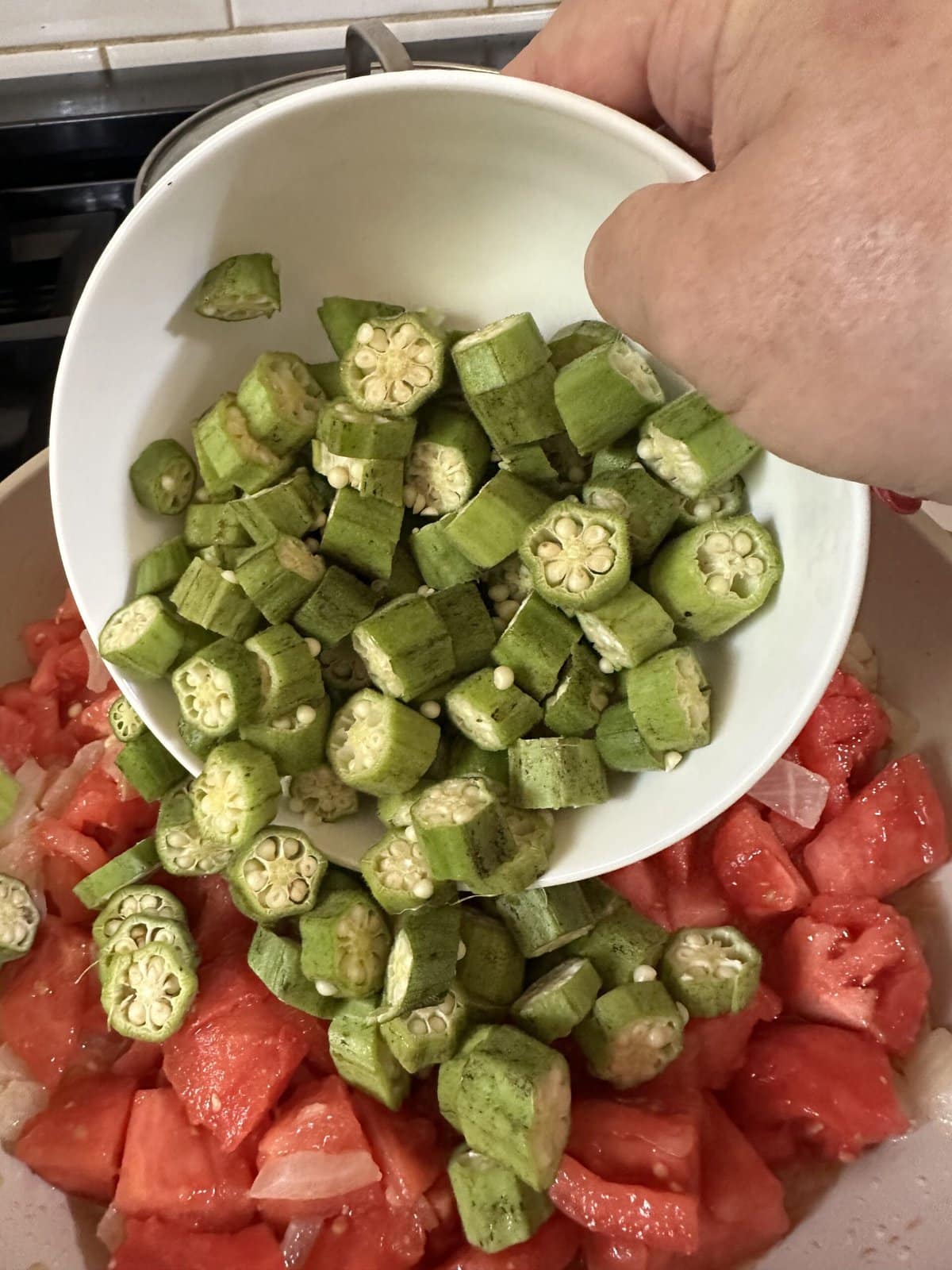 Adding the sliced okra to the tomatoes and onions.