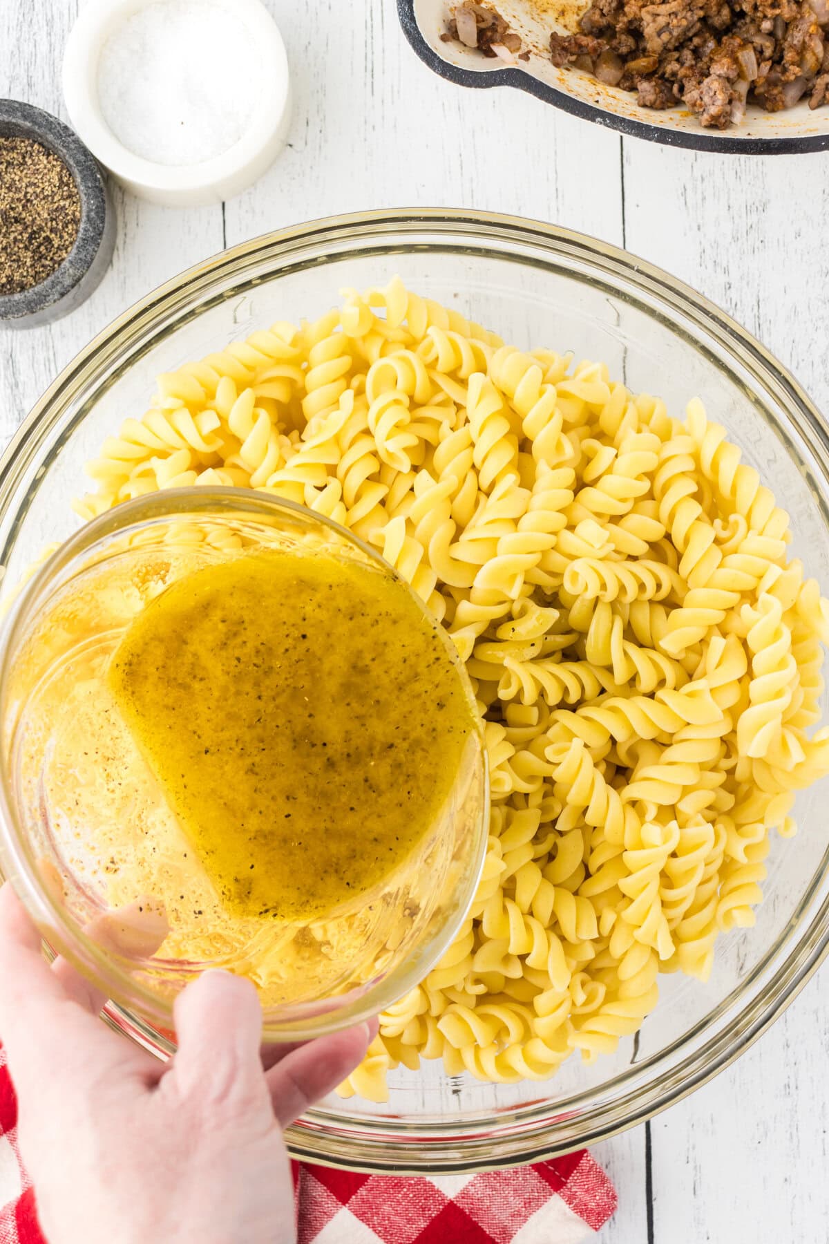 Pouring the dressing over the pasta in a large mixing bowl.