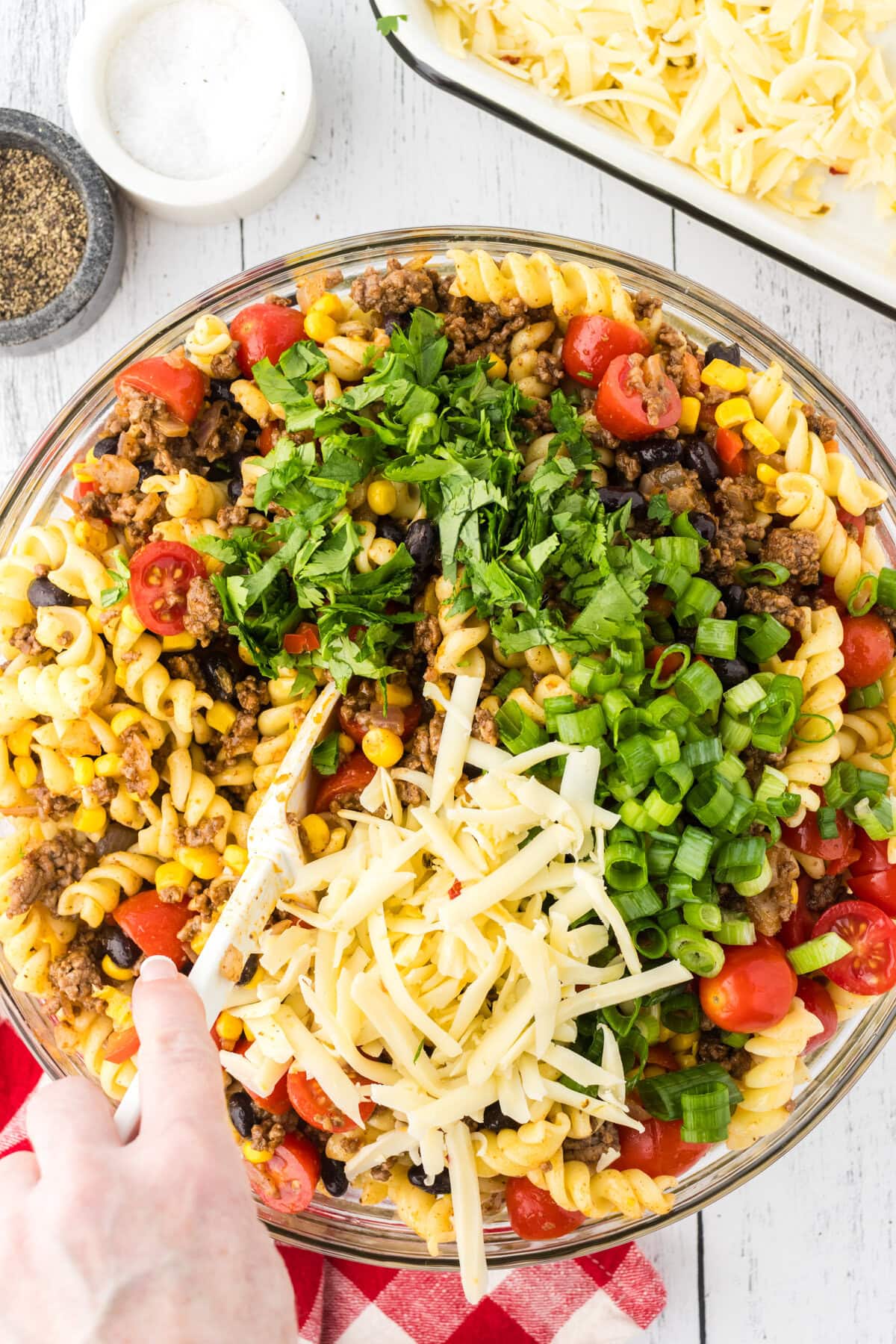 Combining the Texas pasta salad with cheese, green onion, and cilantro.