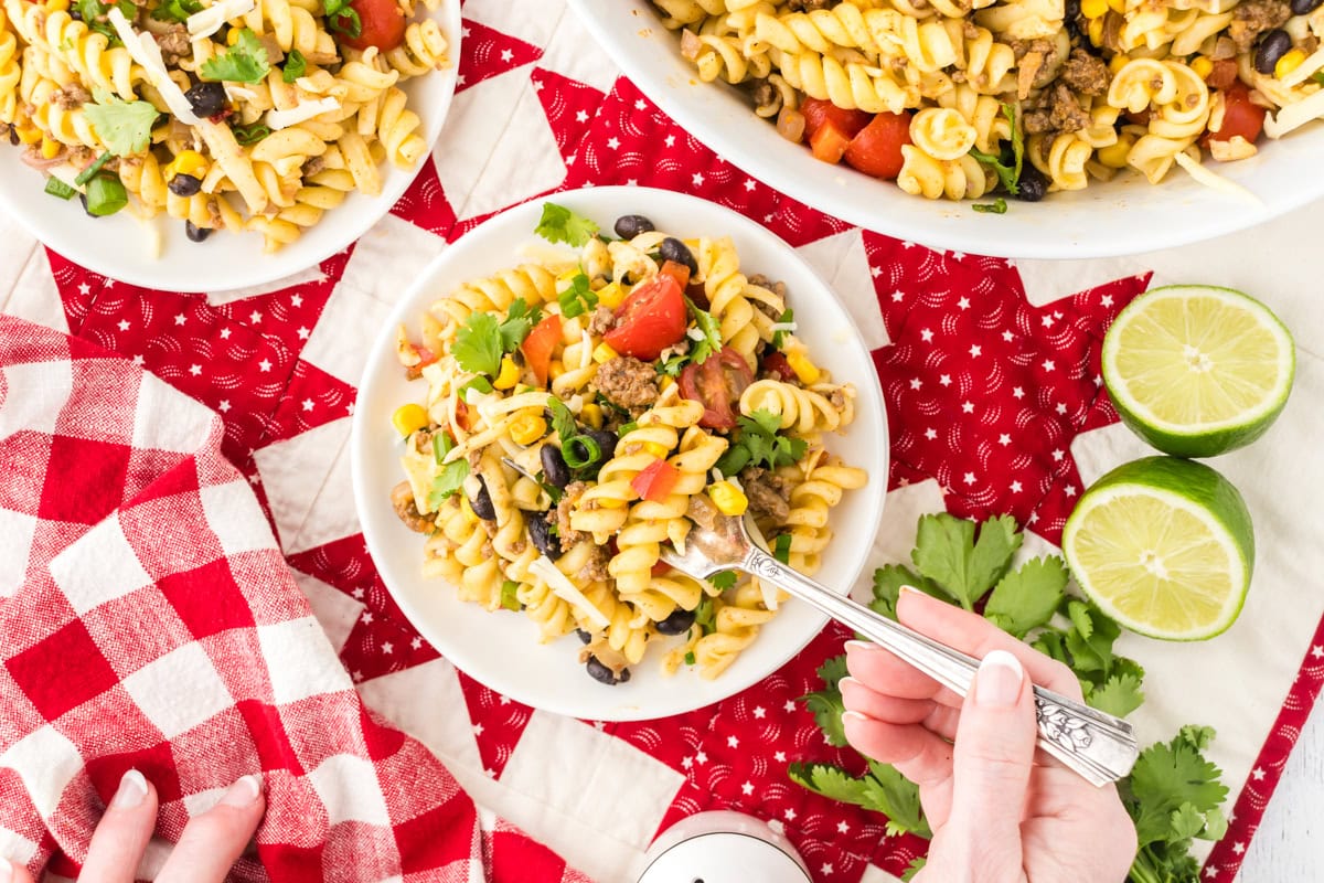 Texas pasta salad in a bowl with a fork next to limes and extra cilantro.