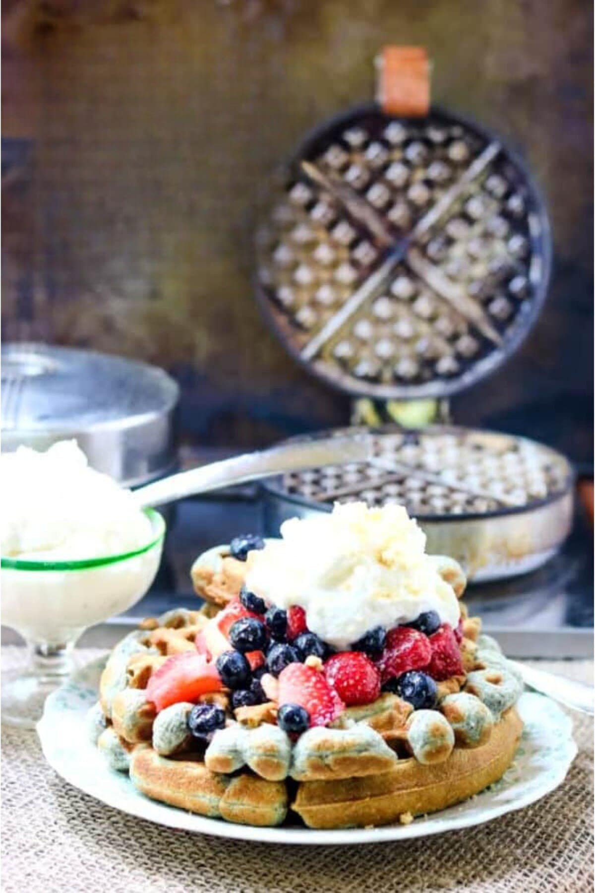 Blue cornmeal waffles with strawberries and blueberries on top.