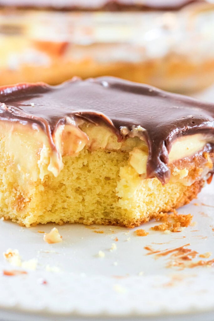 Closeup of Boston Cream Poke Cake with a bite removed to show the layers of cake, pudding, and chocolate.