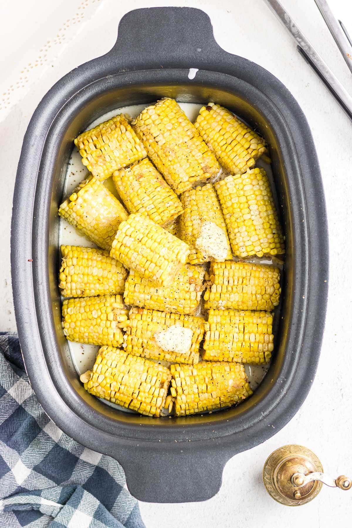 Cooked ears of corn in the slow cooker with butter melting on top.