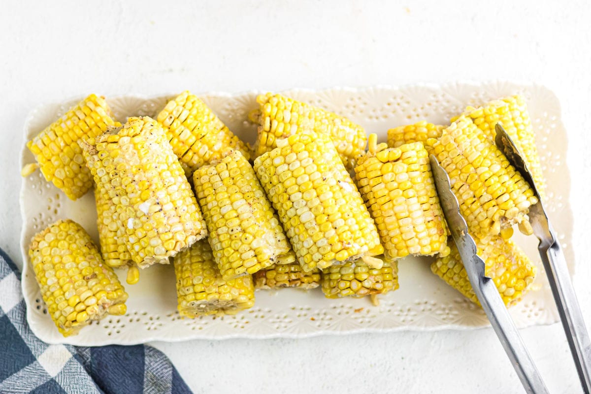 Corn being removed from the serving dish with tongs.