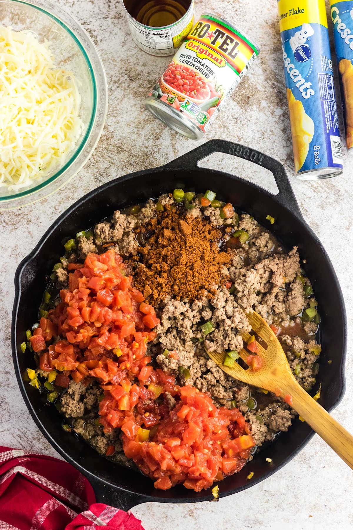 Overhead view of a cast iron skillet with cooked ground beef, taco seasoning and tomatoes in it.