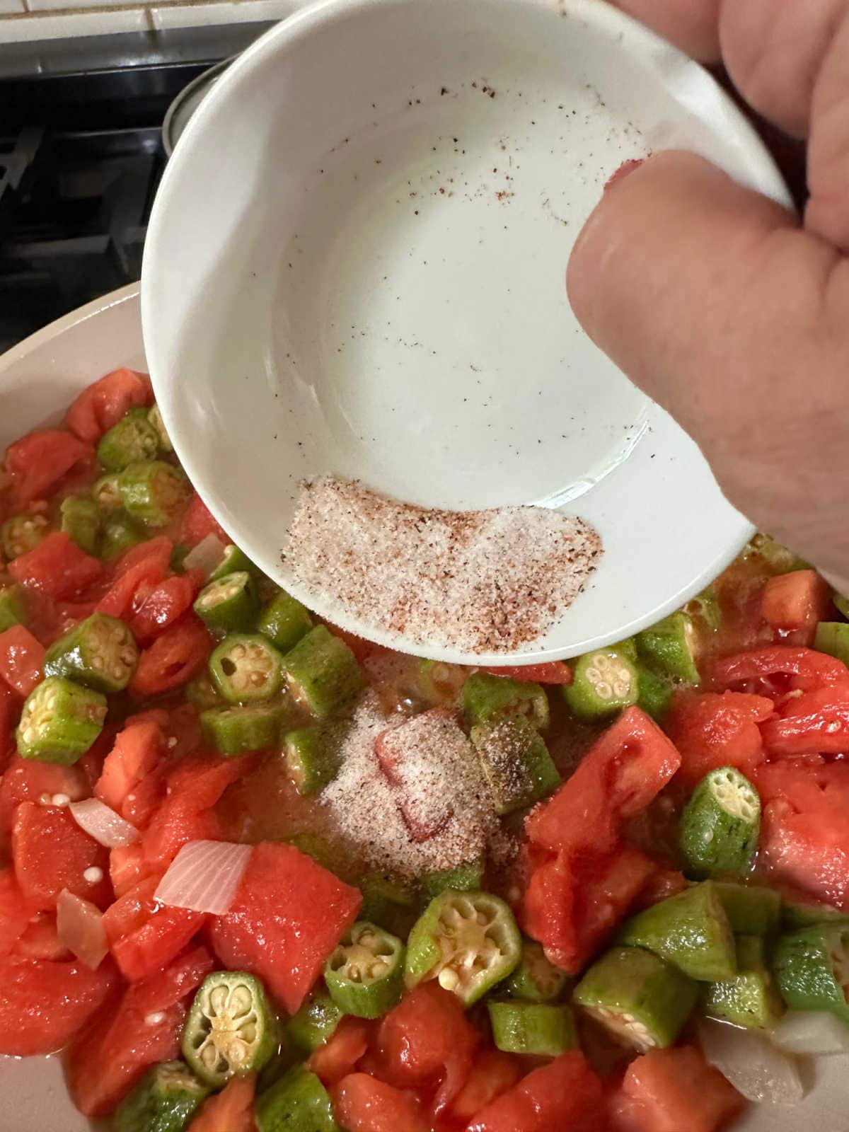 Adding seasoning to the okra and tomatoes.