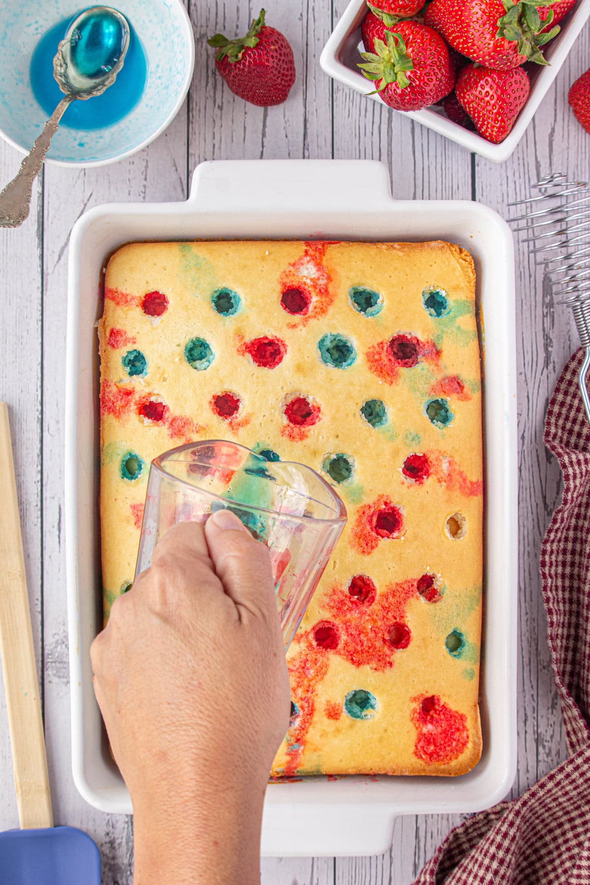 Pouring liquid Jello into the holes that have been poked in the baked cake.