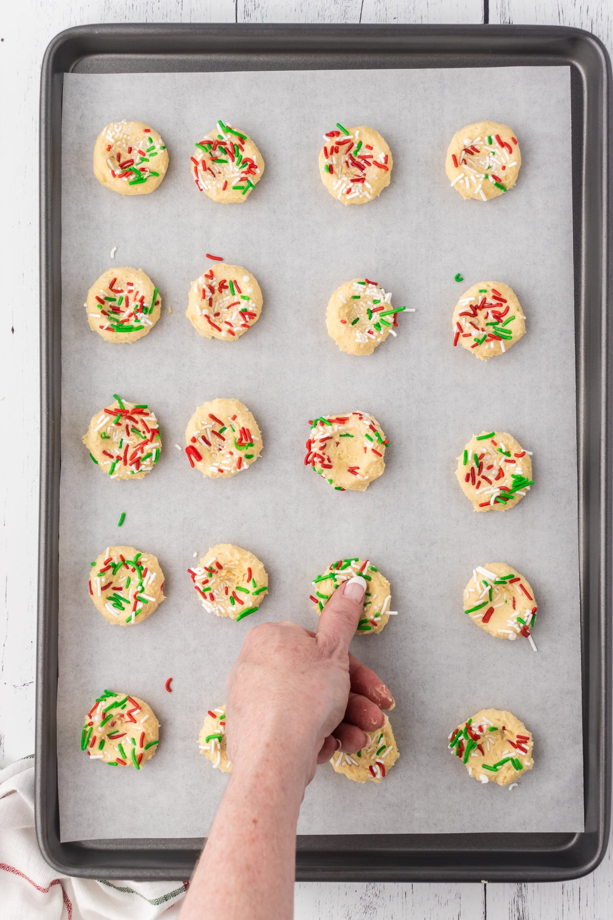 Using a thumb to make an indentation in each cookie dough ball.