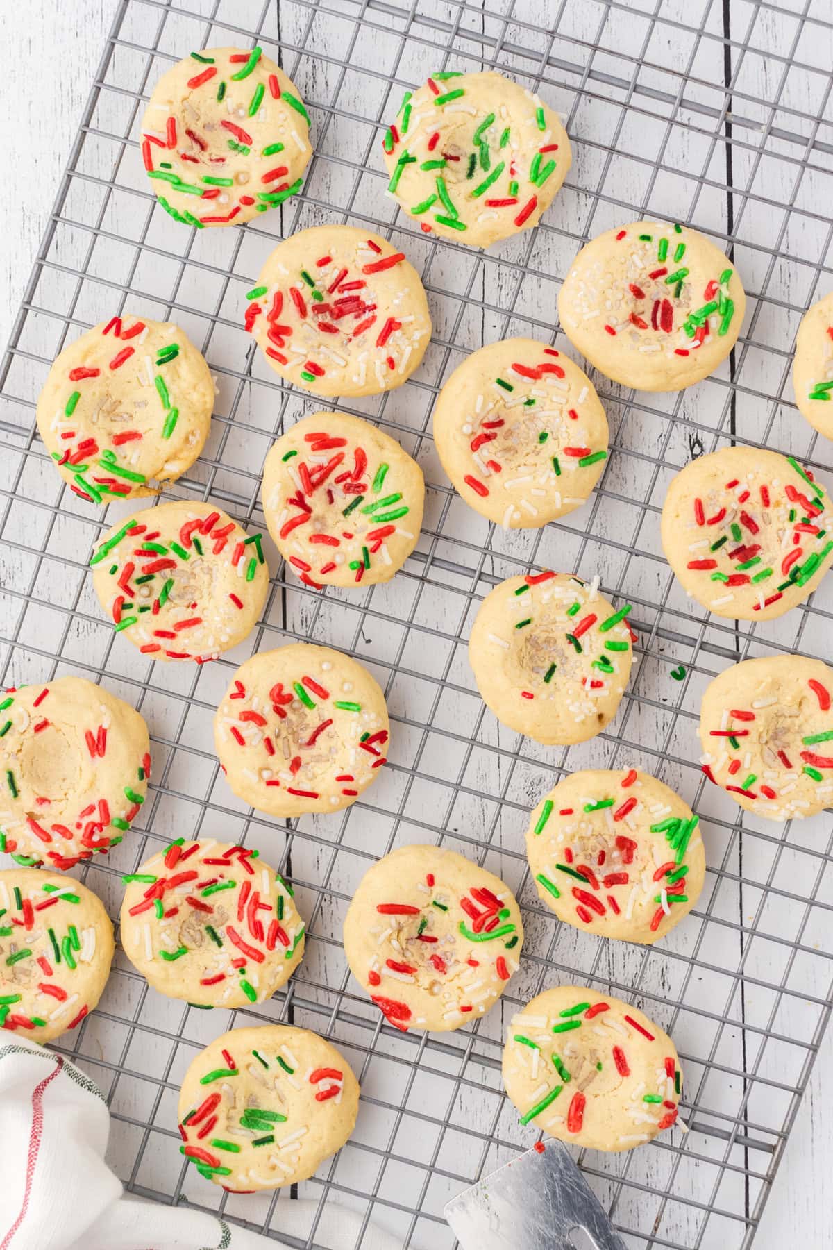 Sprinkled Christmas thumbprint cookies cooling on a rack.