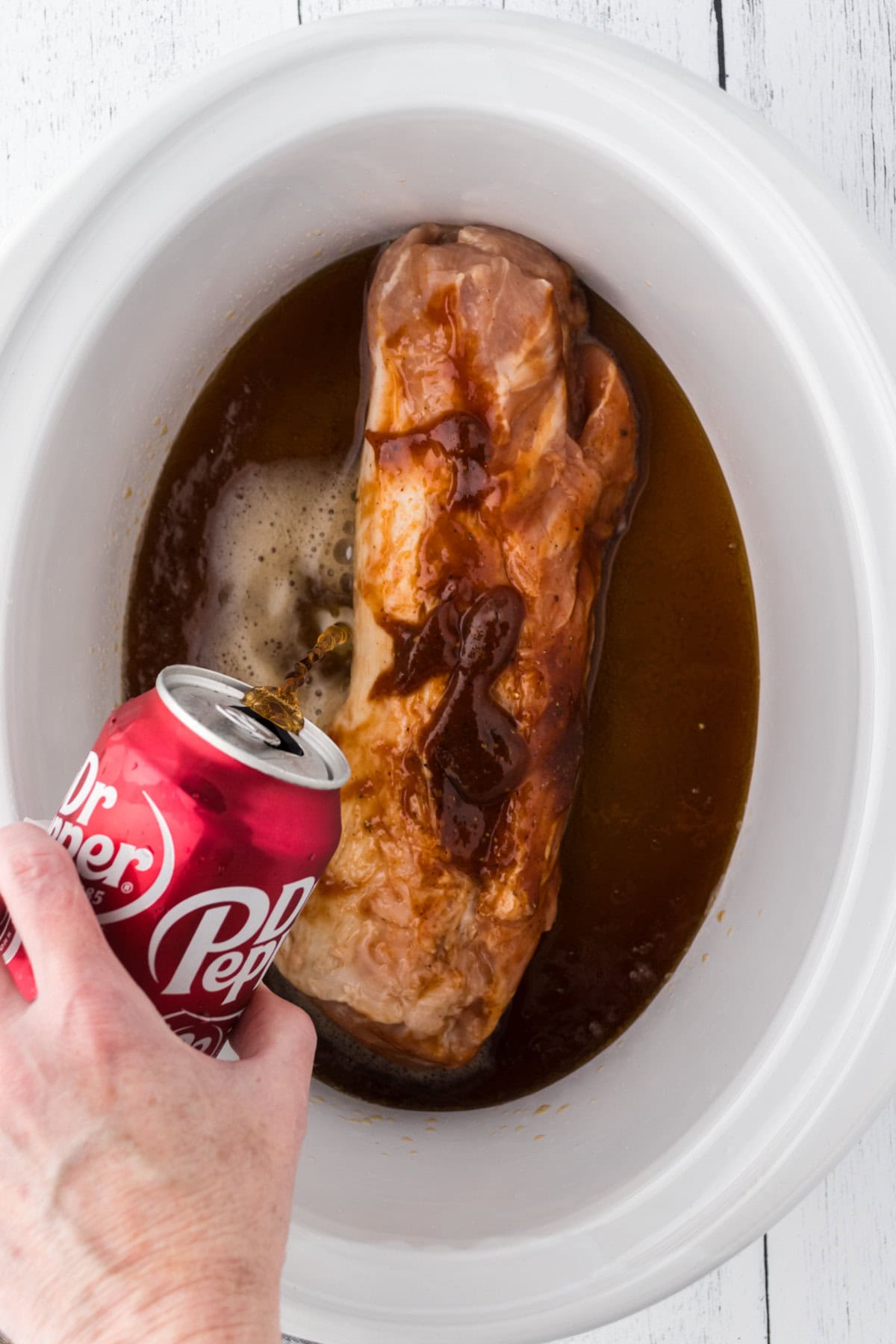 Pouring the can of Dr Pepper into the slow cooker.