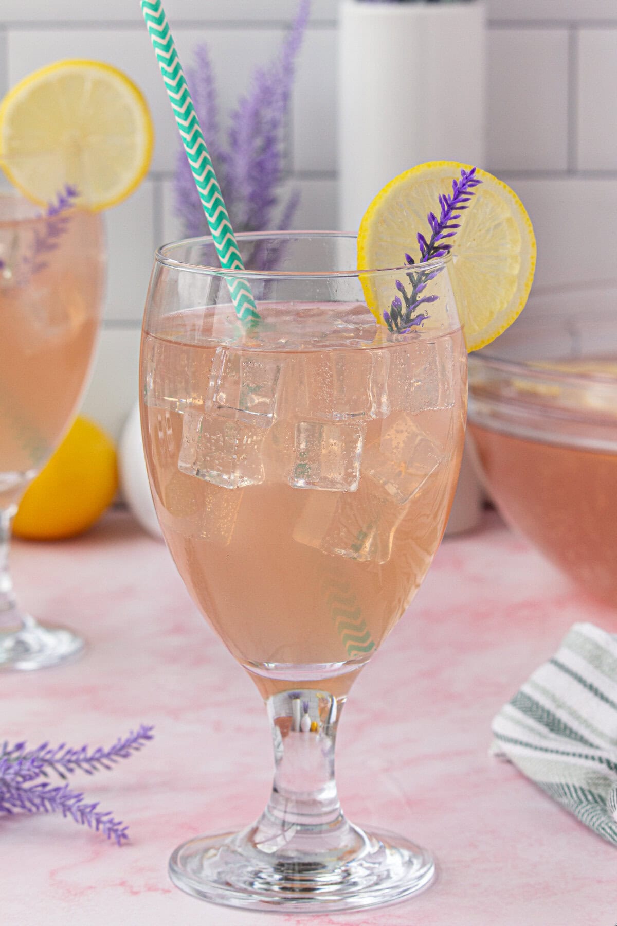 Lavender punch in a stemmed glass with a lavender spring and a lemon garnish.