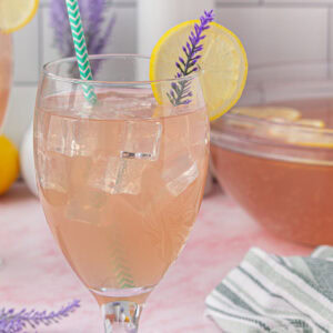 A closeup of a stemmed glaass of lavender punch with a lemon garnish.