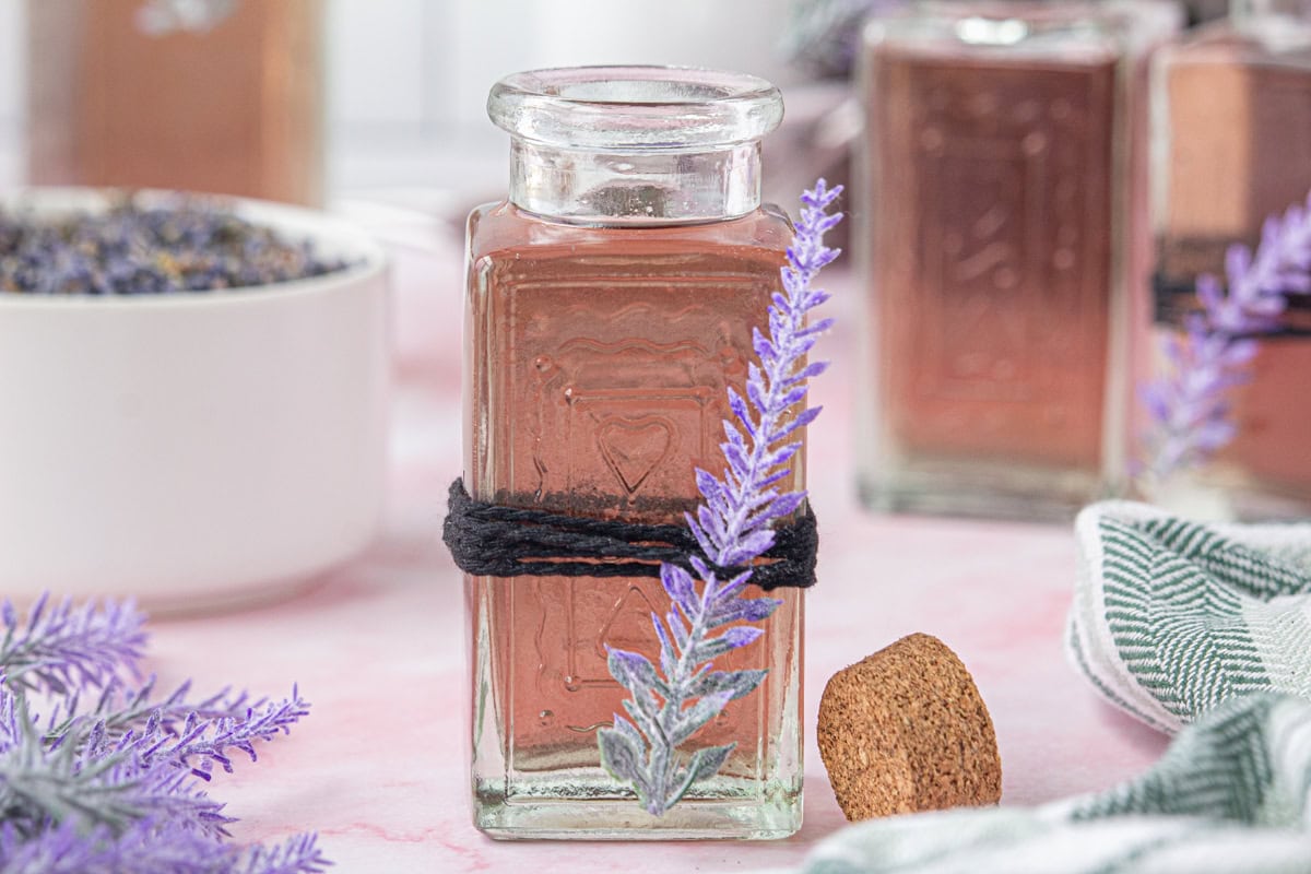 A jar of lavender simple syrup with twine and a lavender sprig.