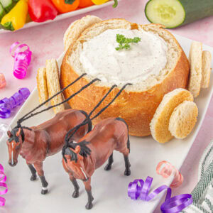 A loaf of round bread has been hollowed out and filled with dip then decorated to look like a coach.