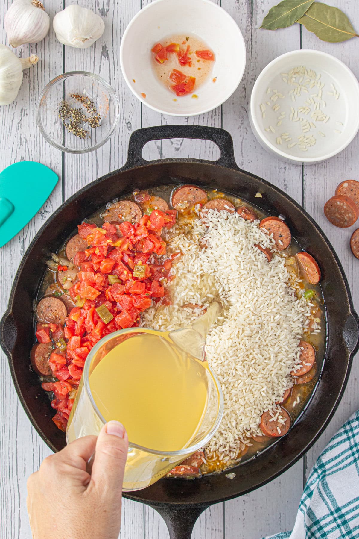 Adding the broth, rice, and tomatoes to the skillet.