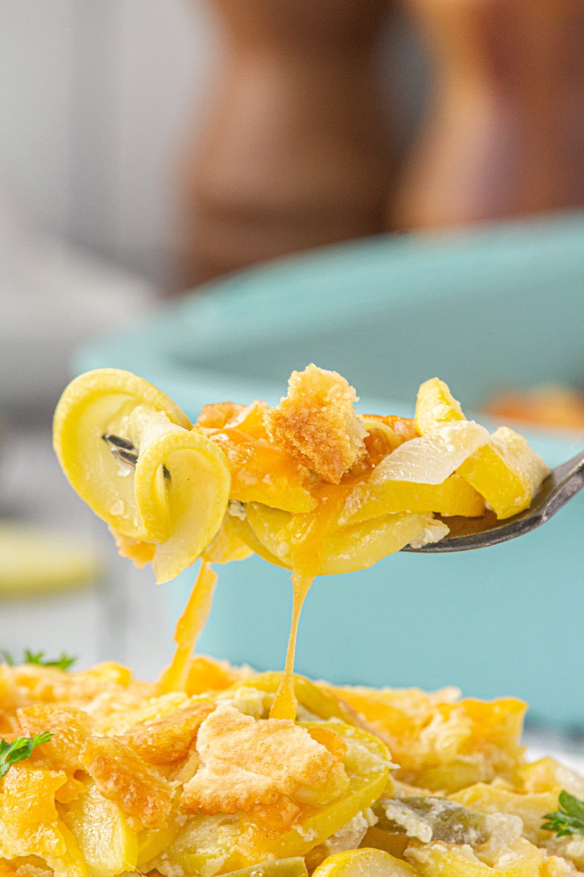A forkful of yellow squash casserole being lifted on a fork with cheesy strings hanging off.