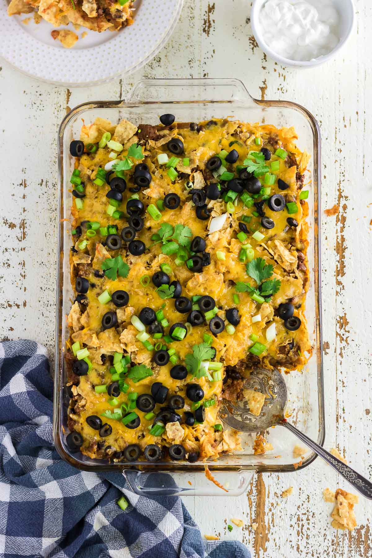 An overhead view of beef nacho casserole with one portion scooped onto a dinner plate.