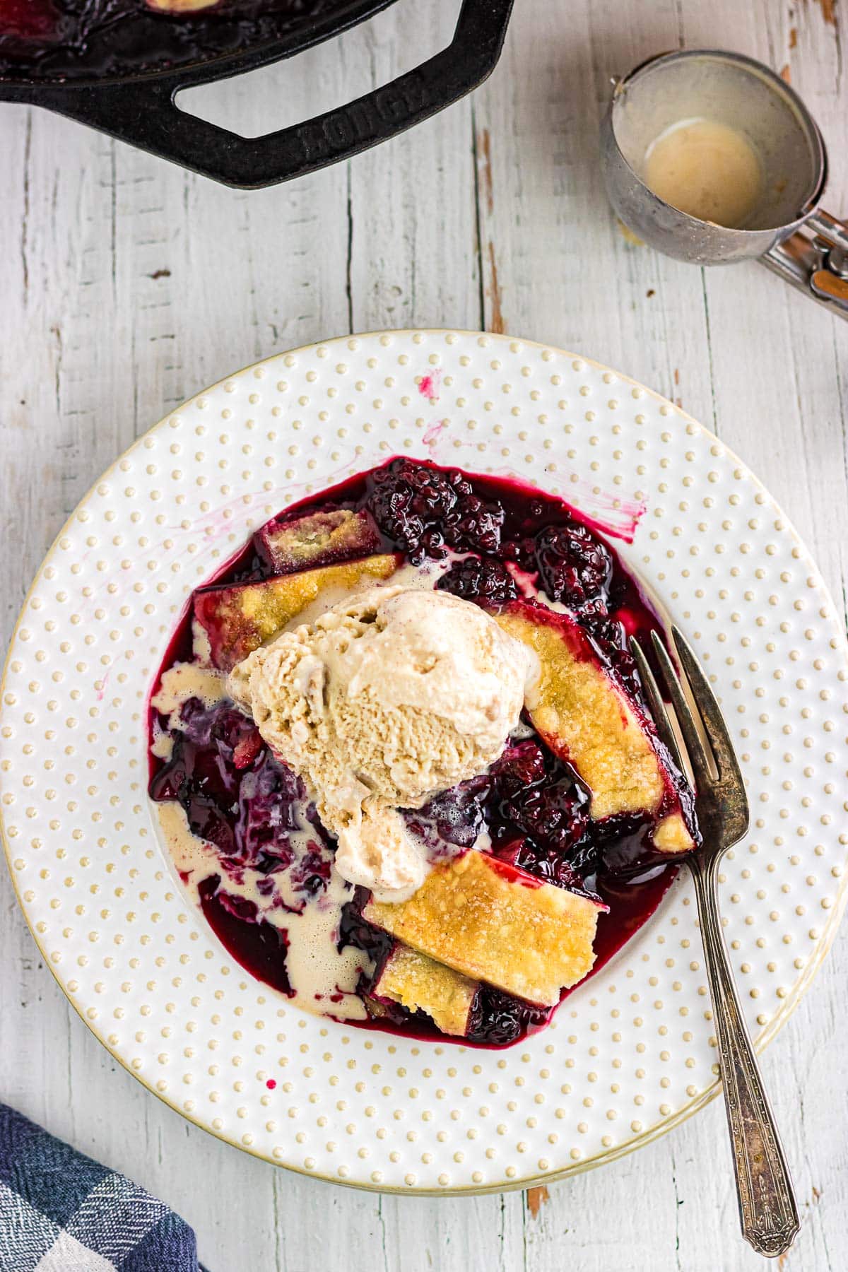 An overhead view of blackberry cobbler with pie crust topped with a scoop of ice cream.