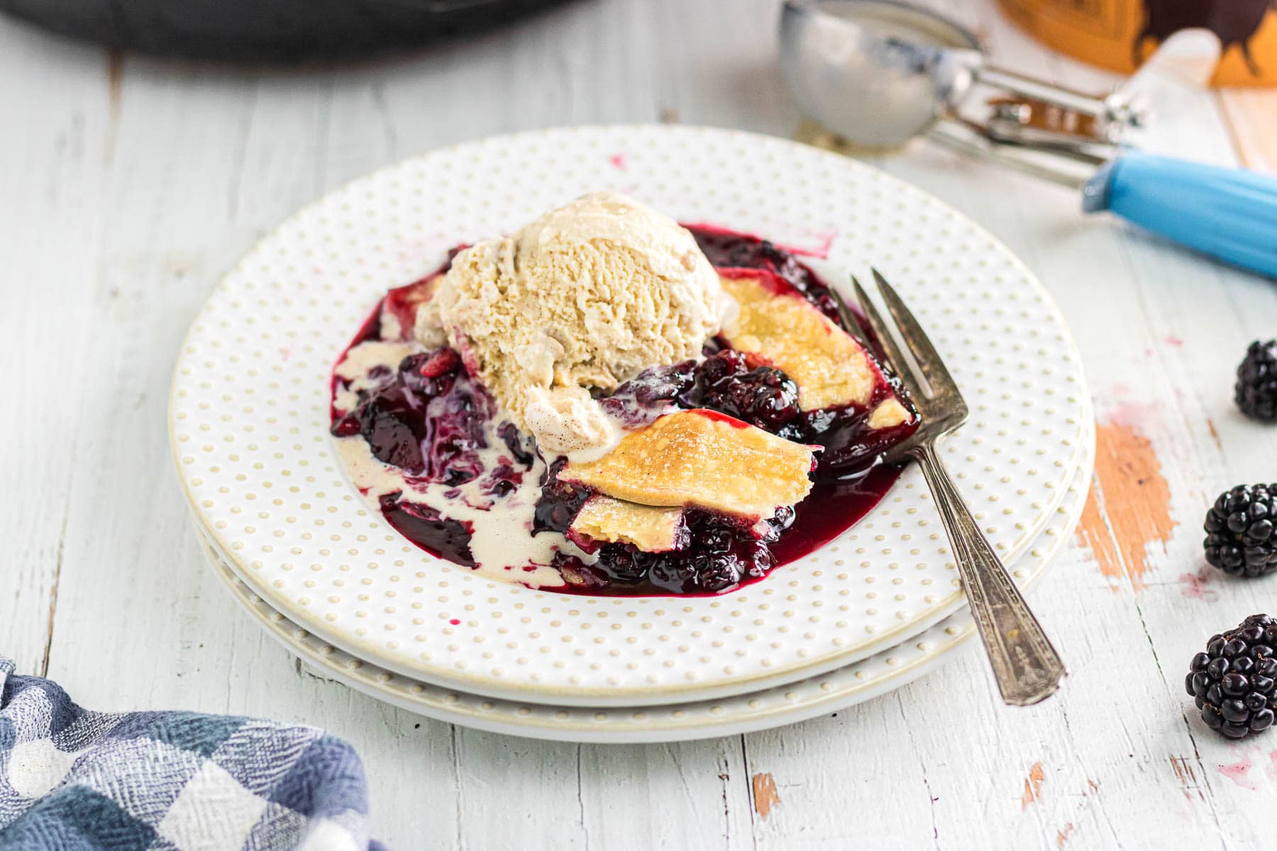 Blackberry cobbler with pie crust in a serving bowl topped with ice cream.