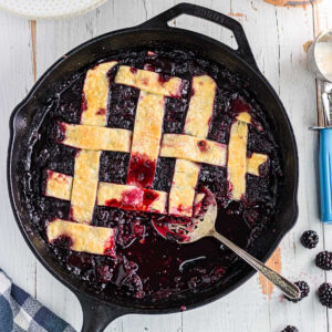 Overhead view of blackberry cobbler with pie crust in an iron skillet.