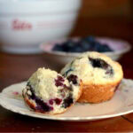 A buttermilk blueberry muffin broken open to show the moist interior.