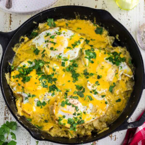 Overhead view of an iron skillet with chilaquiles, melted cheese,and fried eggs.