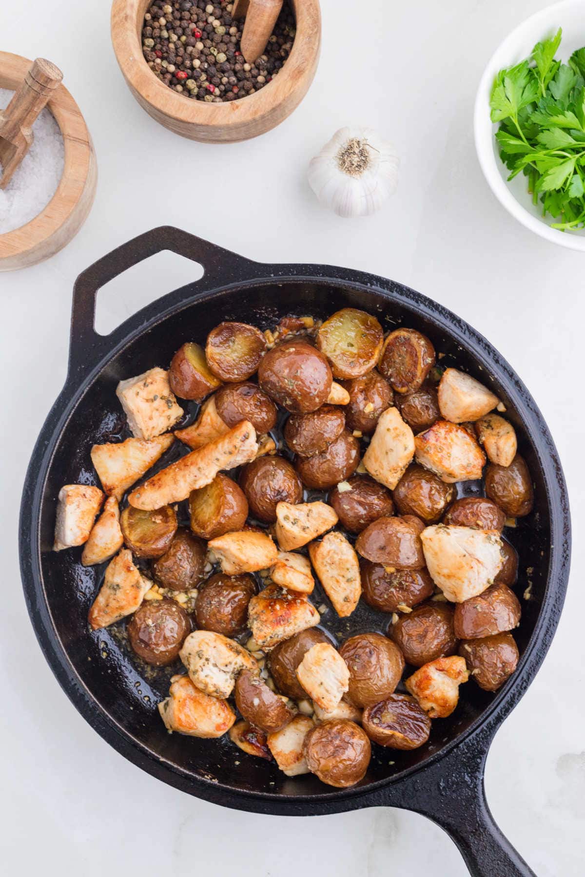 Combing the garlic butter, chicken, and potatoes in the skillet.