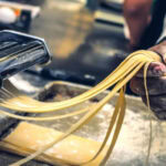 Homemade pasta being cut with a pasta machine.