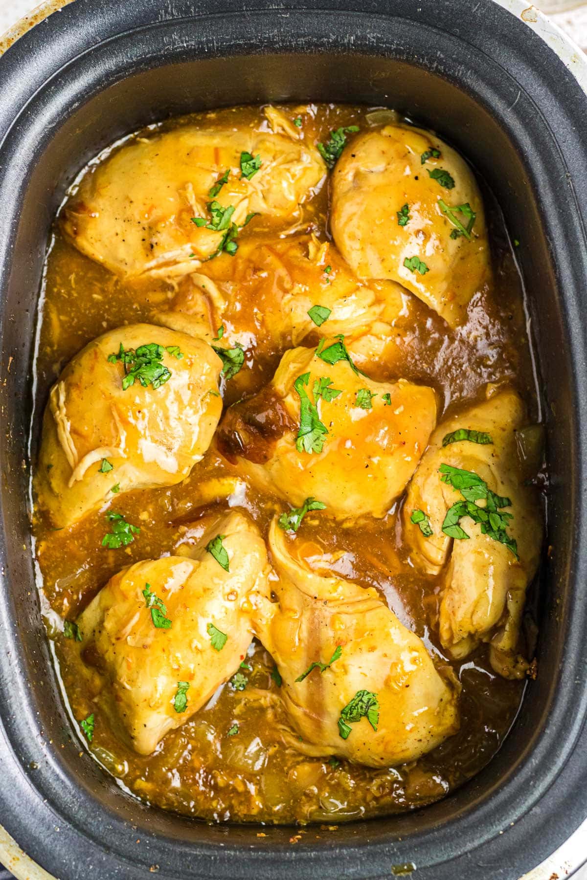 An overhead view of orange chipotle chicken in a slow cooker.