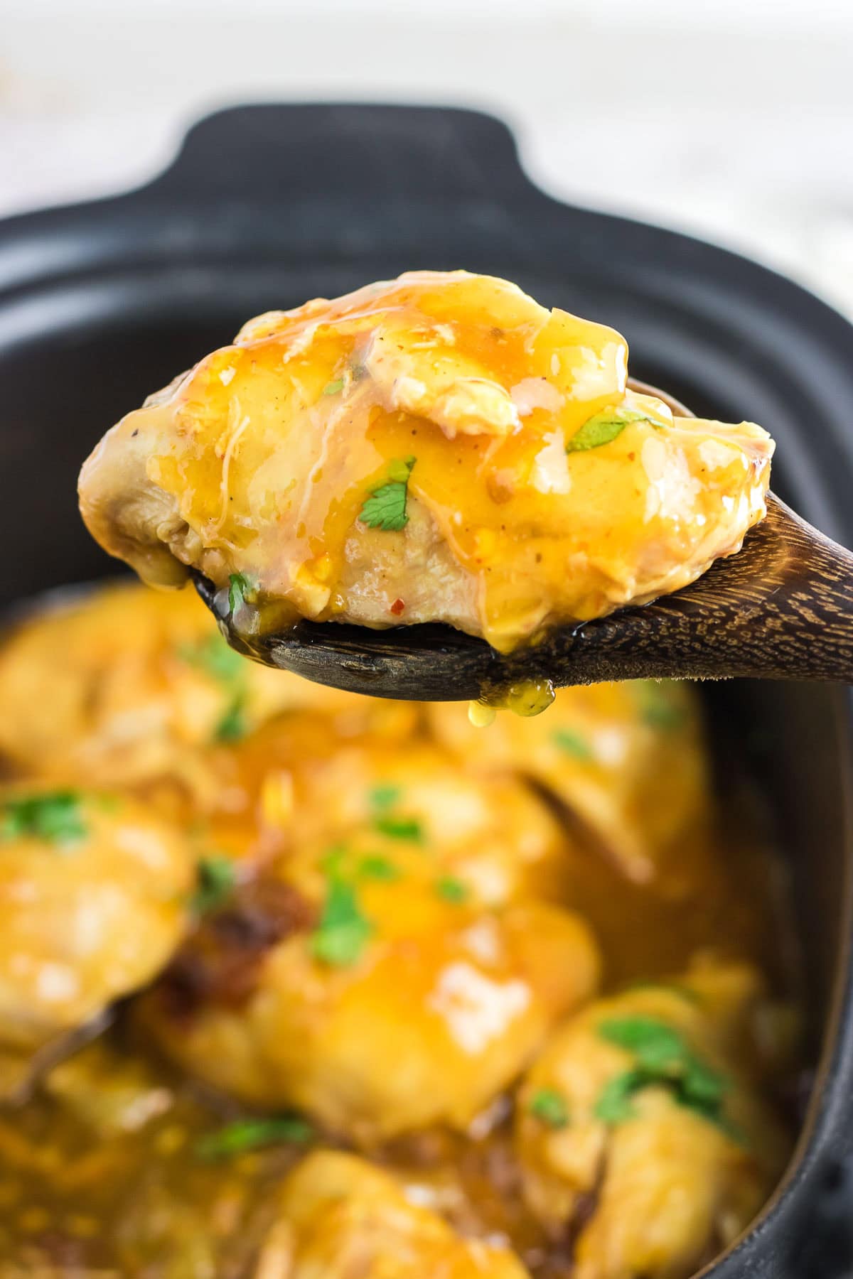 An up-close view of a scoop of orange chipotle chicken on a wooden spoon.