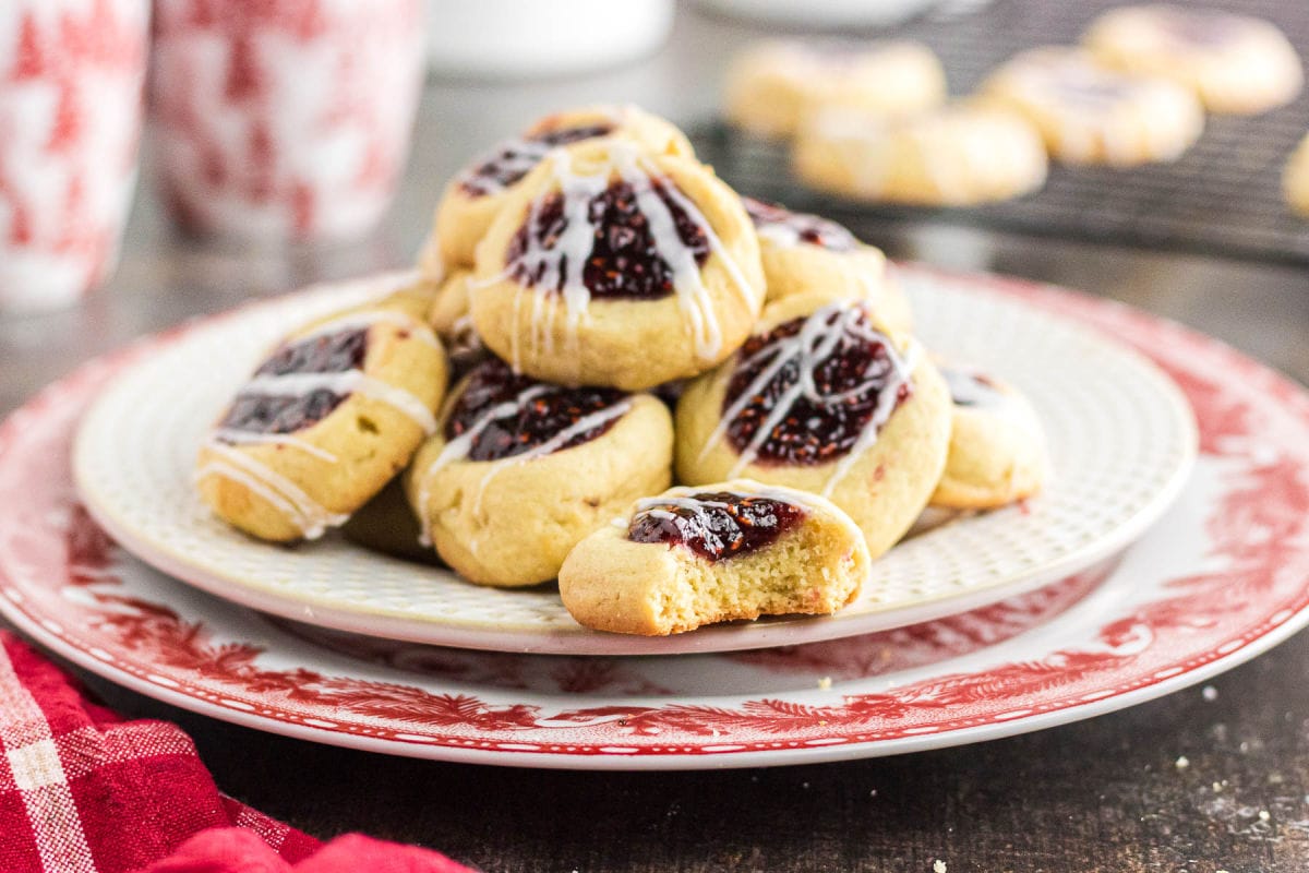 A close-up view of raspberry jam thumbprint cookies on a plate.