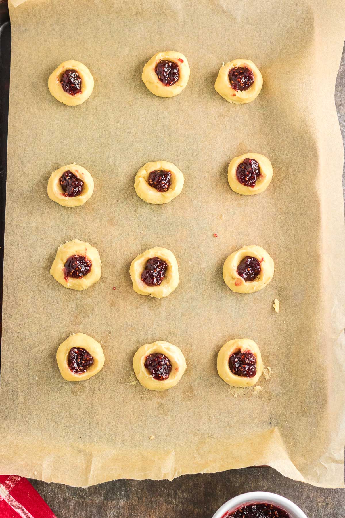 Cookies on a baking sheet filled with raspberry jam.