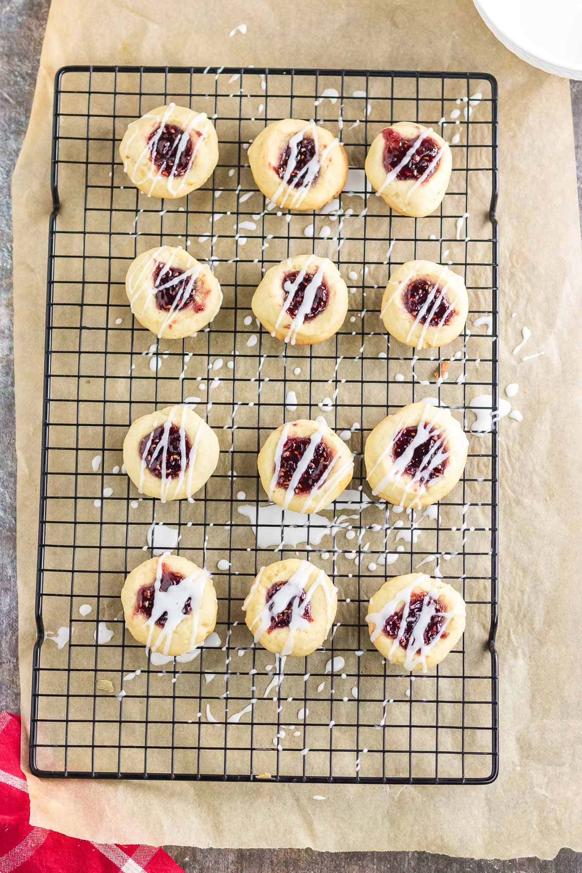 Raspberry thumbprint cookies on a cooling rack drizzled with white chocolate.