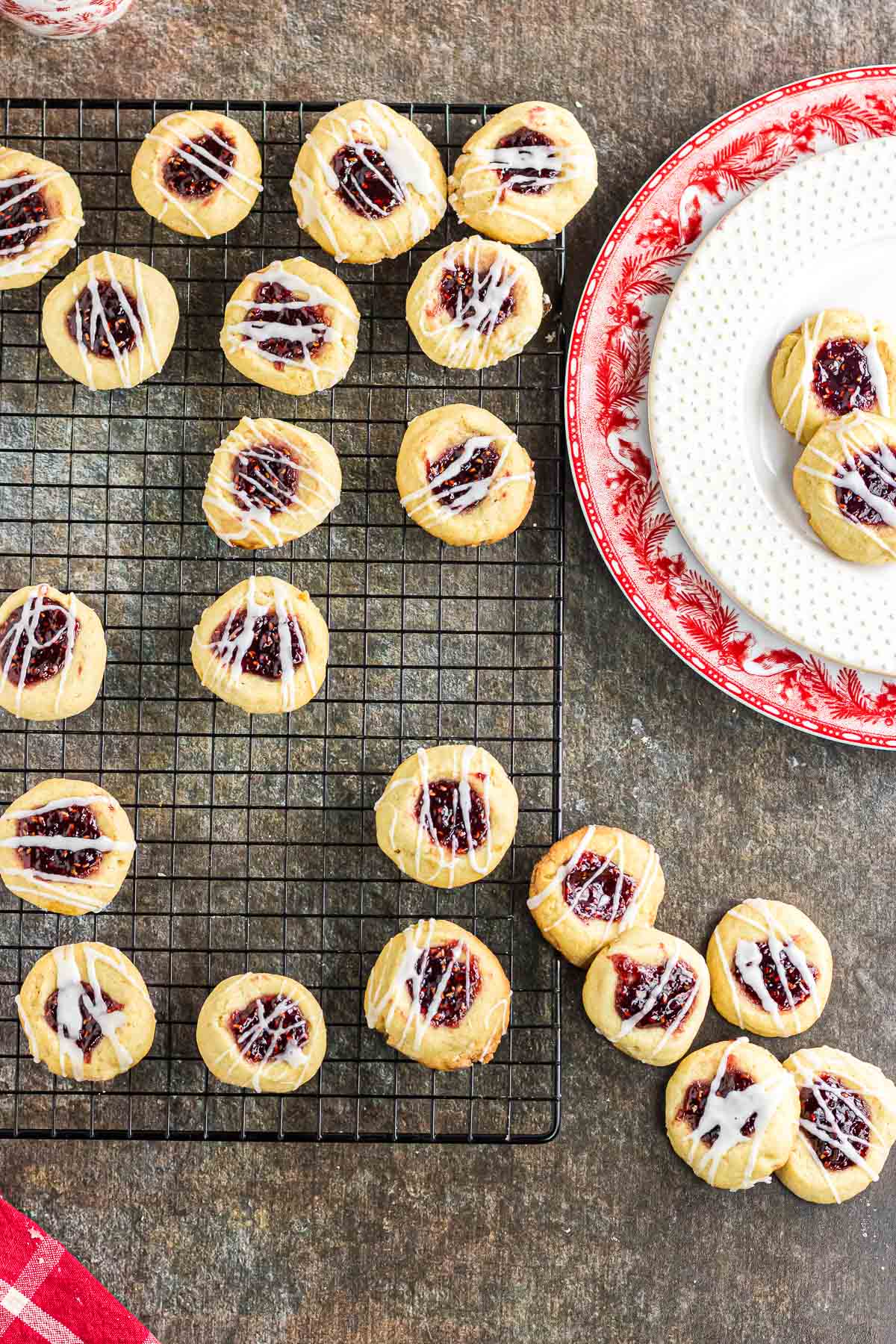 An overhead photo of raspberry jam thumbprints on a wire cooling rack and a plate.