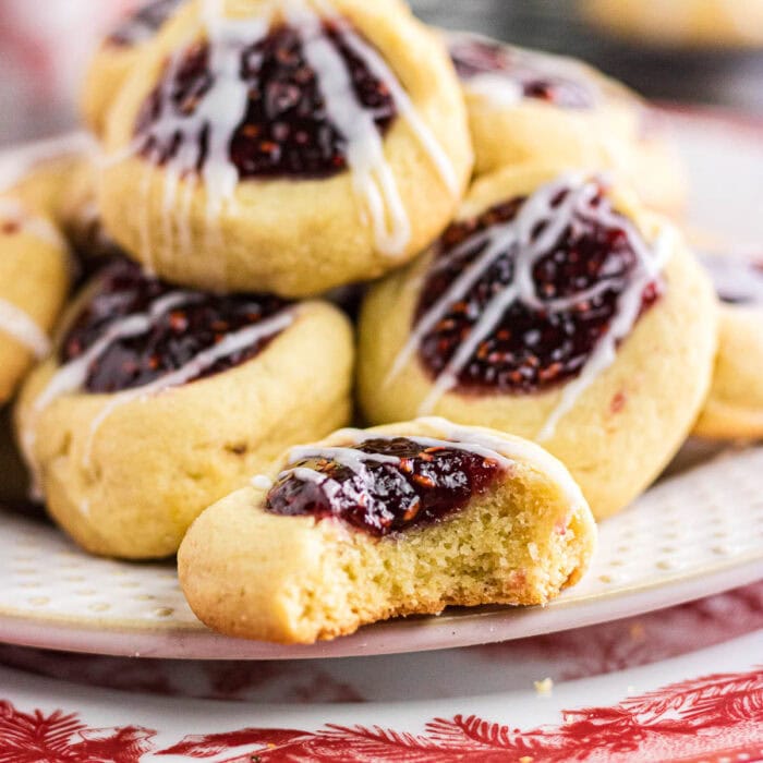 Raspberry thumbprint cookies drizzled with white chocolate stacked on a plate.